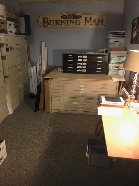 Room filled with flat map cases, cabinets, and boxes. On the wall sign says "Burning Man Museum".