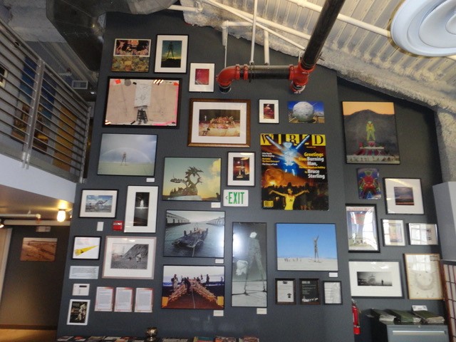 A wall of images from the 1990s, depicting history of Burning Man. Includes magazine covers and photographs.