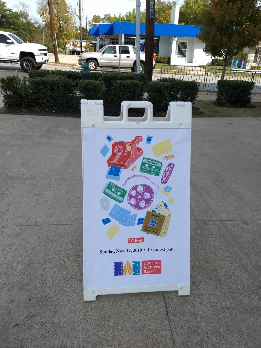 Sandwich sign with graphic on top three quarters of sign than text below that says "It's Free! Sunday, Nov. 17, 201- - 10 a.m. – 2.pm. Houston Archives Bazaar"