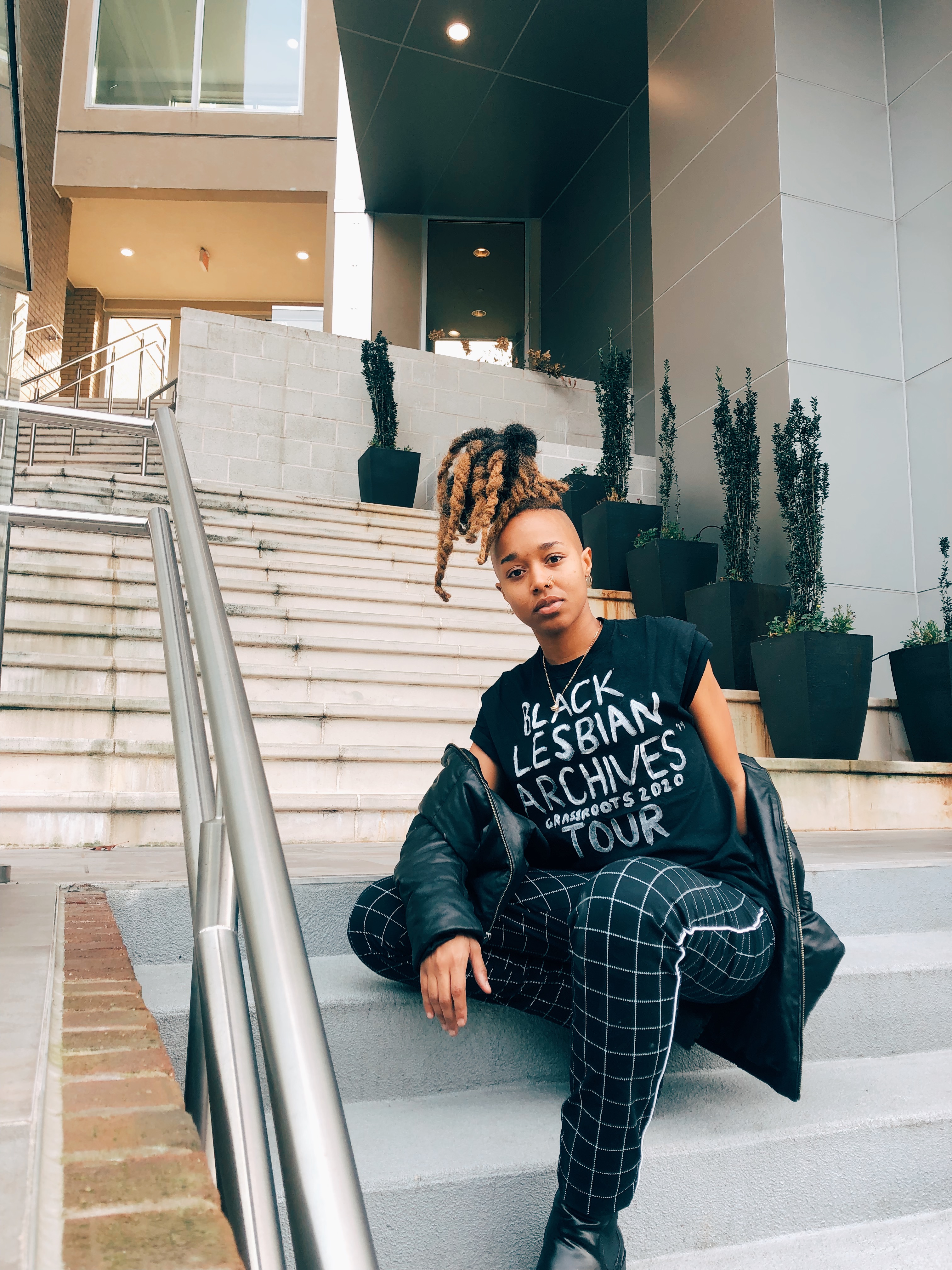 Krü Maekdo sitting on steps with tee that says "Black Lesbian Archives Grassroots 2020 Tour"