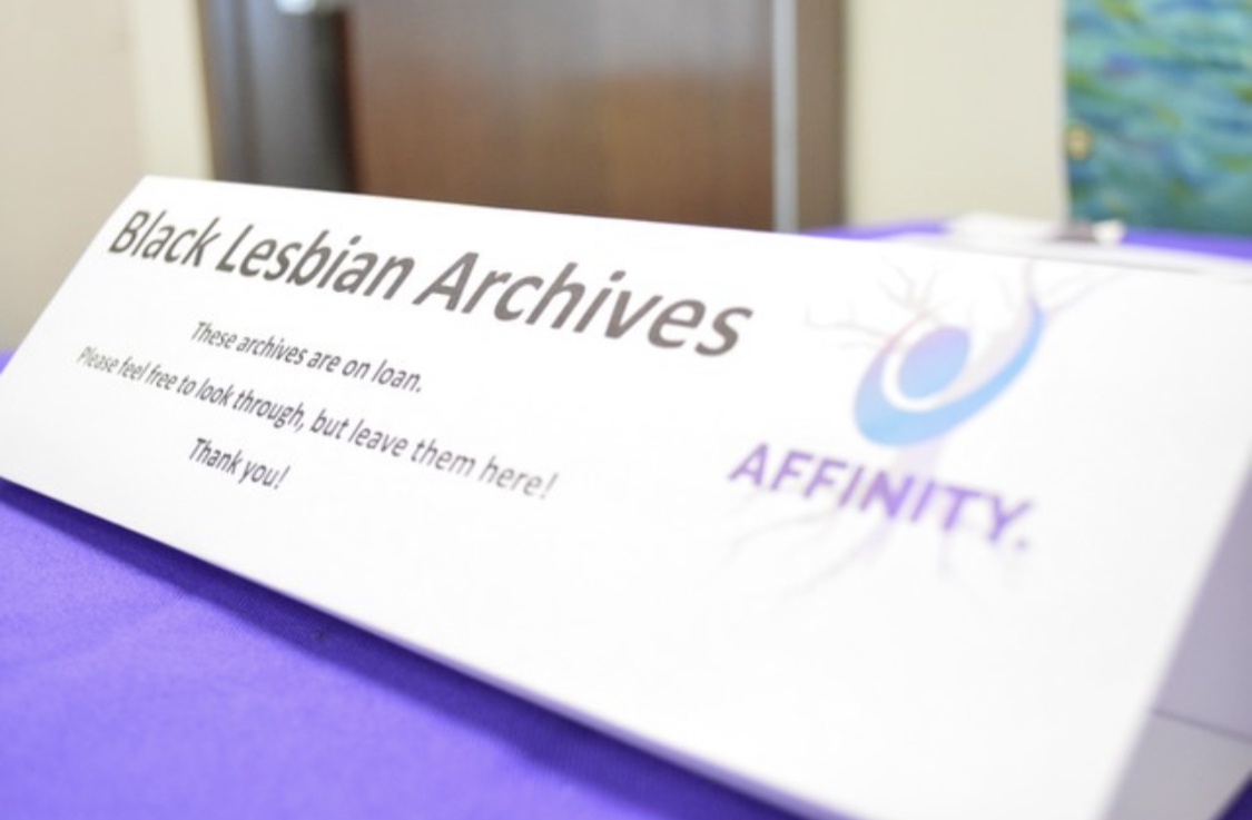 Table top sign that says "Black Lesbian Archives. These archives are on loan. Please feel free to look through, but leave them here! Thank you! With Affinity and logo on the right.