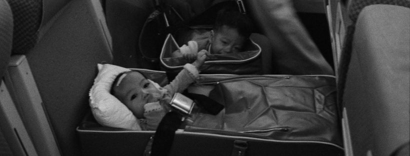 Interior of a plane with babies strapped in carriers and crew in the aisles